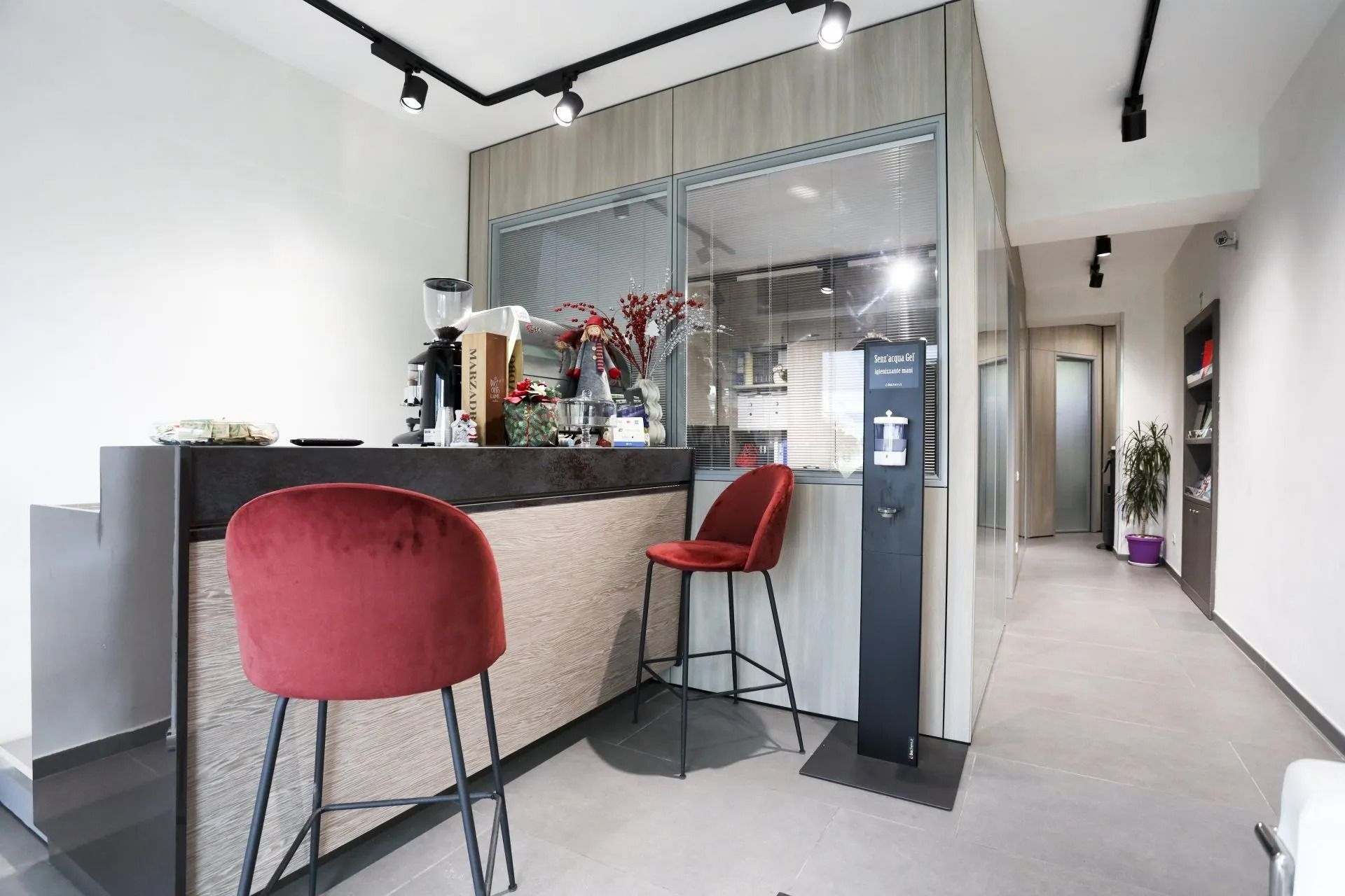 Area bar con sgabelli rossi. Attrezzatura per il caffè sul bancone. Il corridoio prosegue sulla destra.