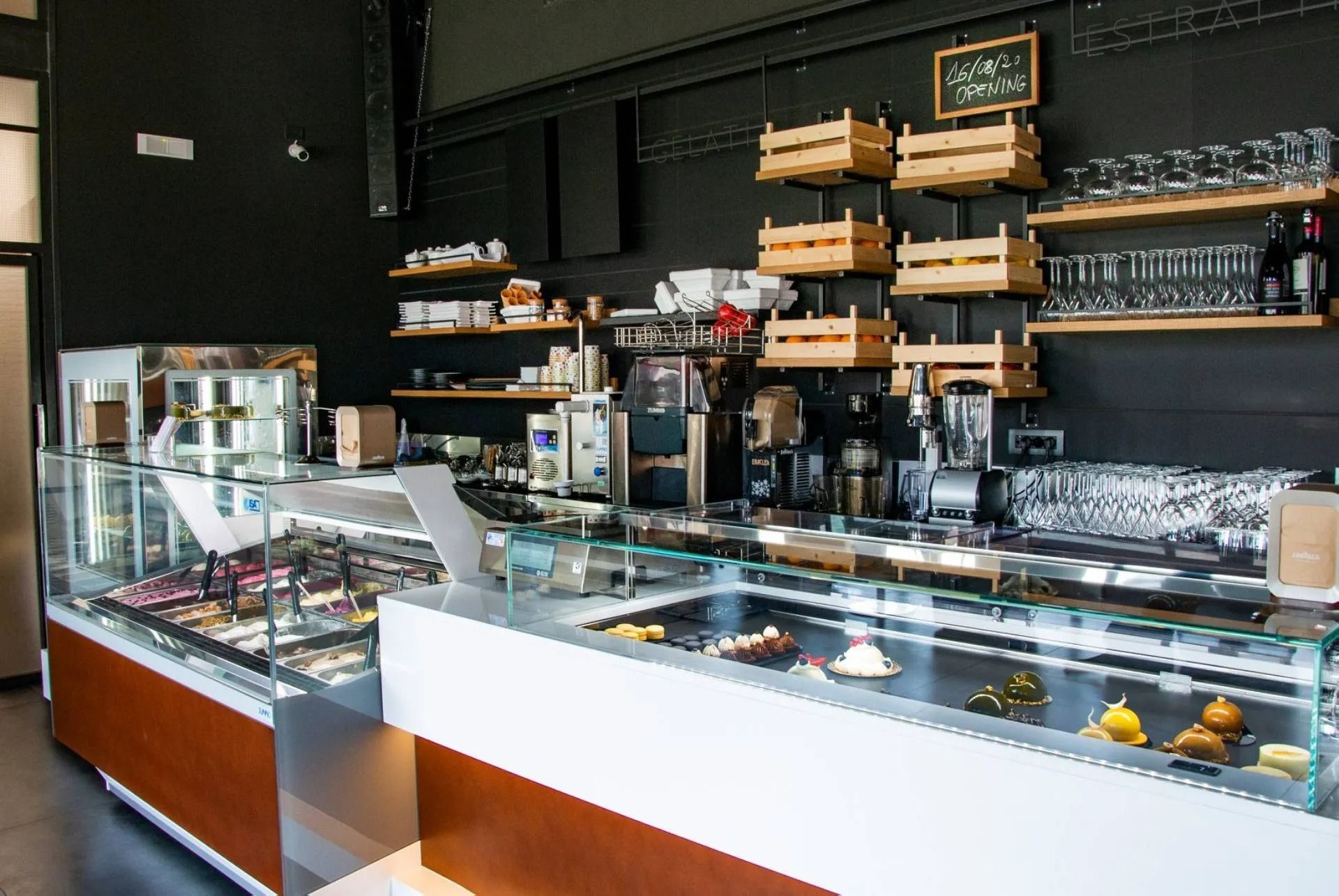 Interno di un bar con vetrina di dolci e gelati, pareti nere e scaffali in legno.