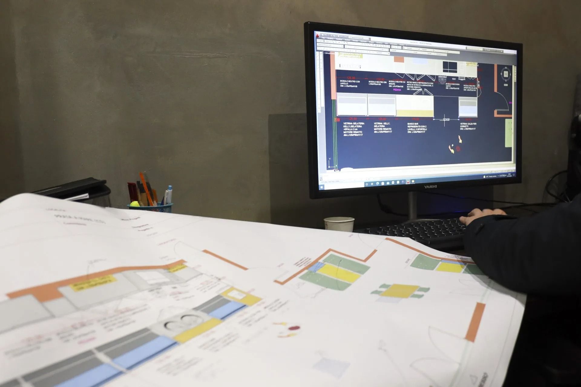 Persona che lavora al computer e rivede i progetti architettonici alla scrivania.