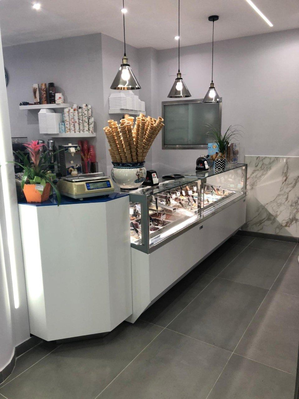 Interno di una gelateria con vetrina, coni e lampade a sospensione.