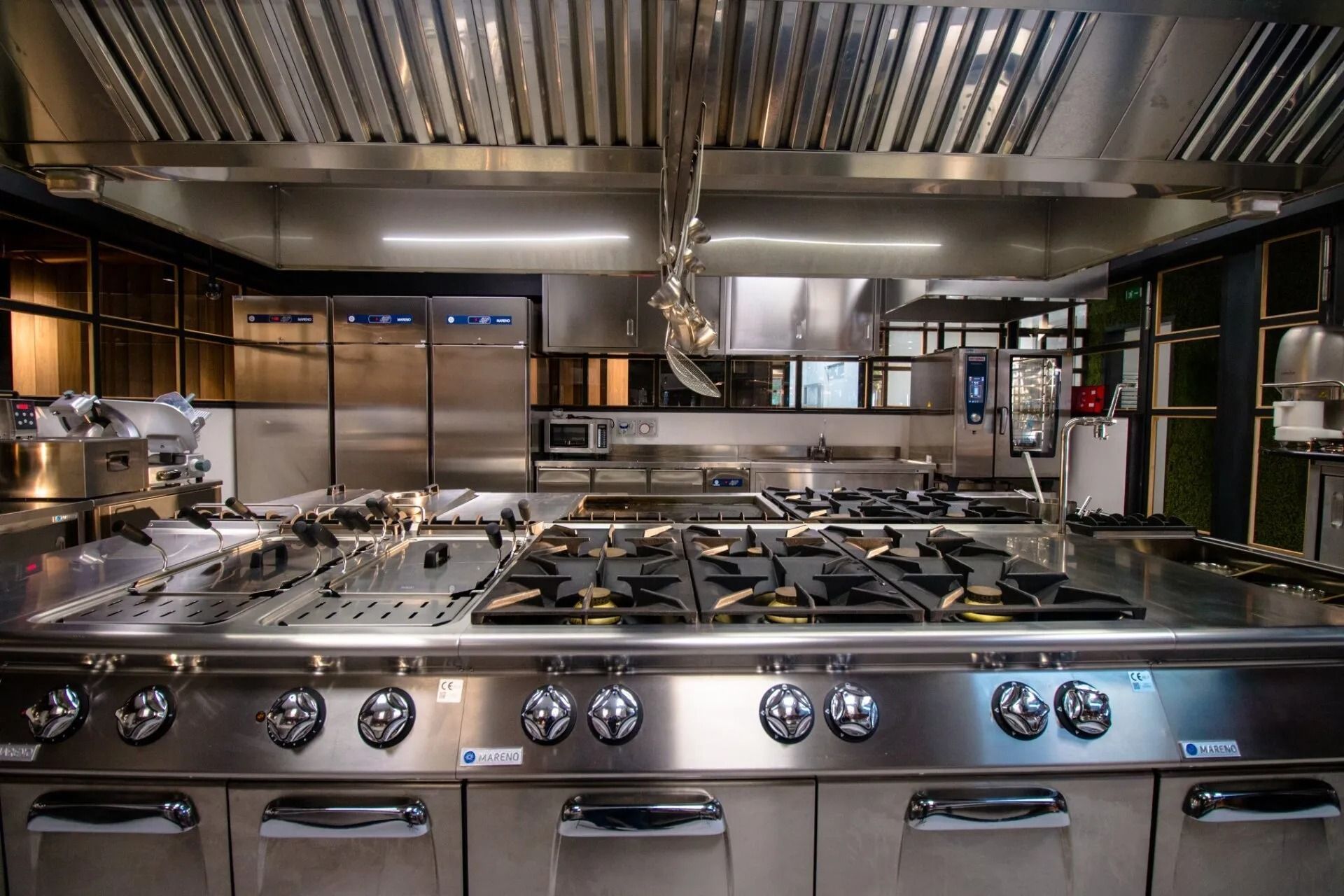 Cucina commerciale con elettrodomestici in acciaio inossidabile, tra cui fornello, cappa e frigorifero.