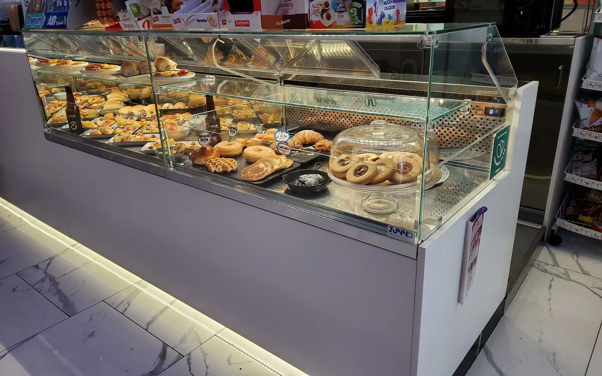 Vetrina di pasticceria con vari prodotti da forno. Bancone bianco con vetrata.