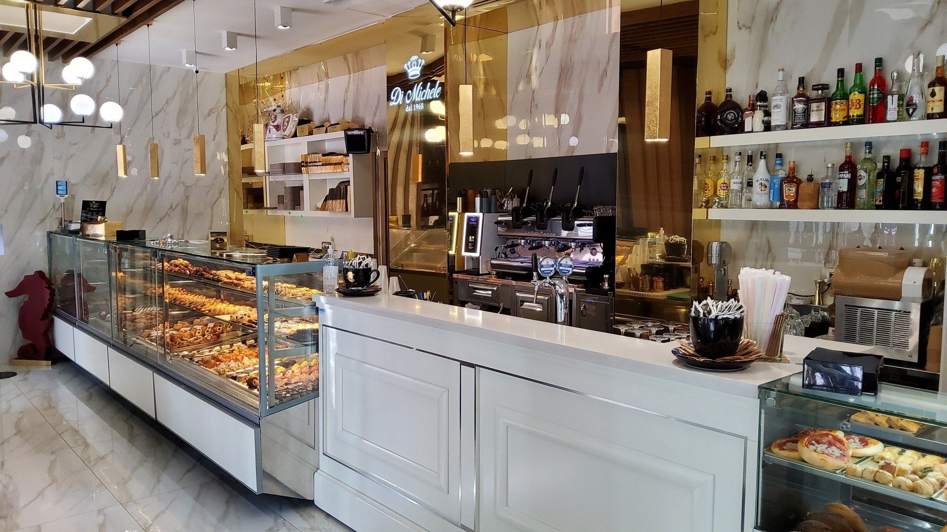 Un luminoso interno da bar con vetrina per dolci, macchina per il caffè e zona bar.
