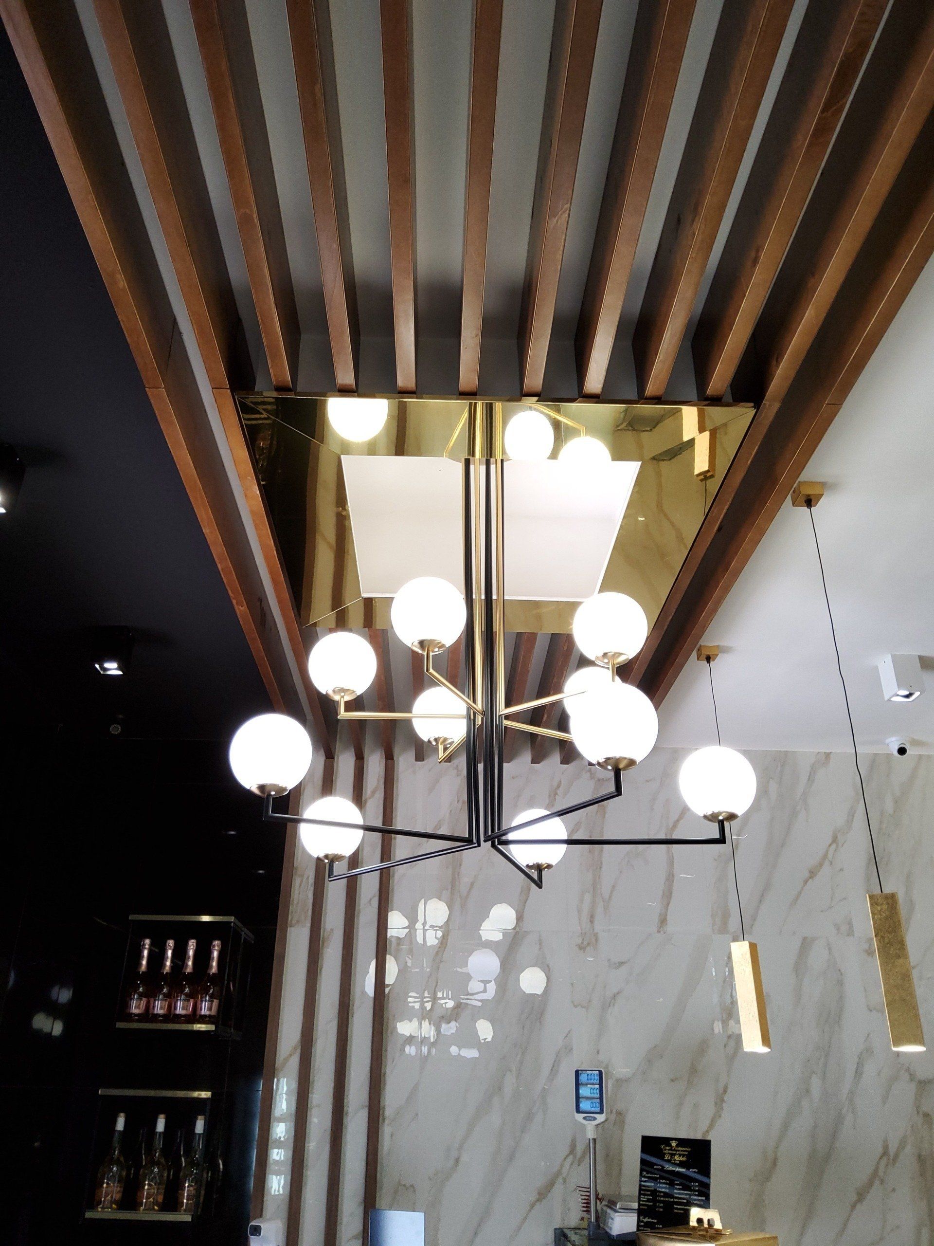 Un lampadario con luci a globo è appeso sotto un soffitto a doghe di legno. Le pareti sono in marmo con accessori moderni.