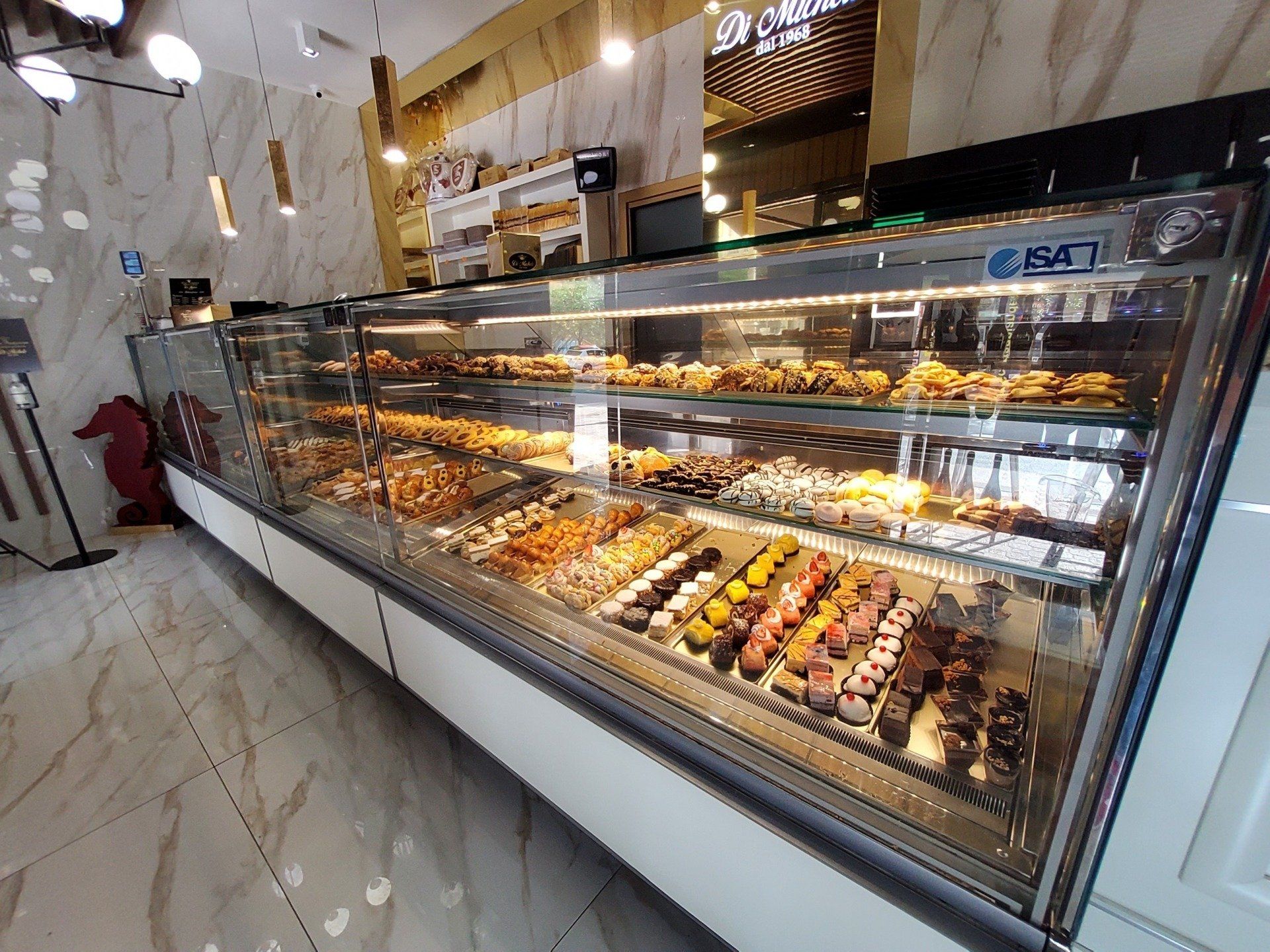 Una vetrina di una panetteria piena di pasticcini e dolci, illuminata da luci soffuse.