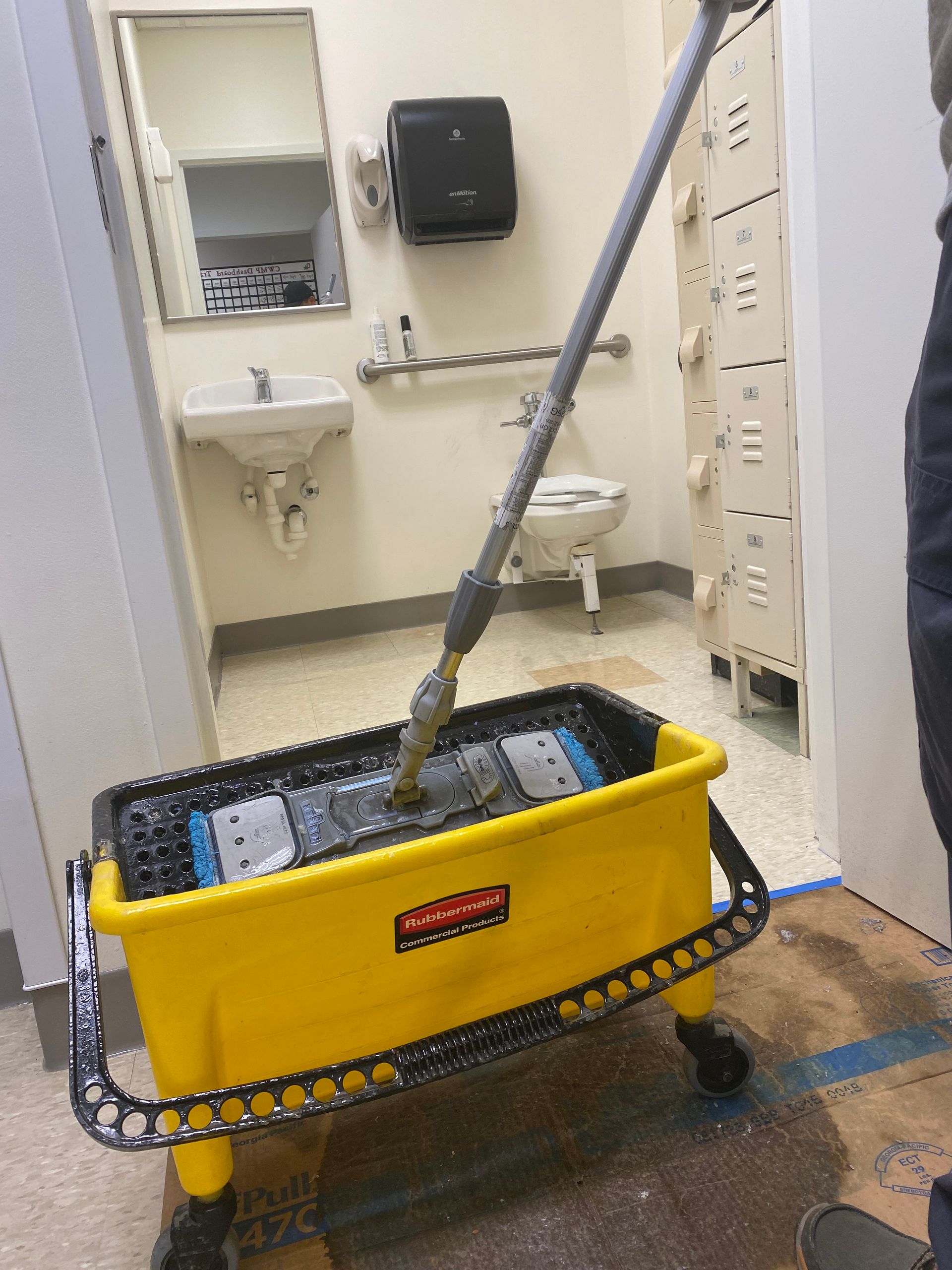 A mop is in a yellow bucket in a bathroom