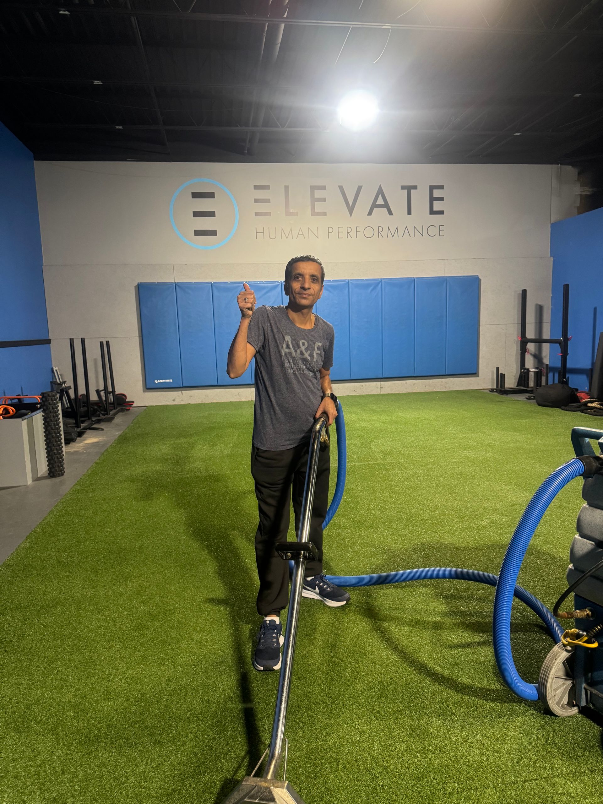 Person wearing yellow gloves sprays and wipes down a white desk with a blue cloth in an office setting.