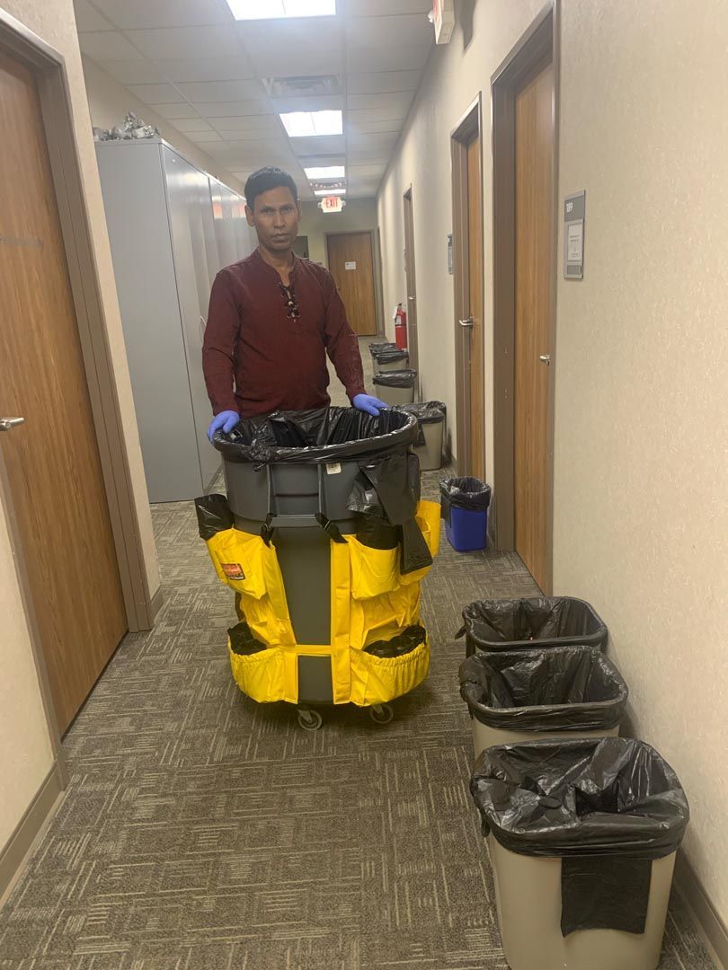 A man is pushing a yellow trash can down a hallway.