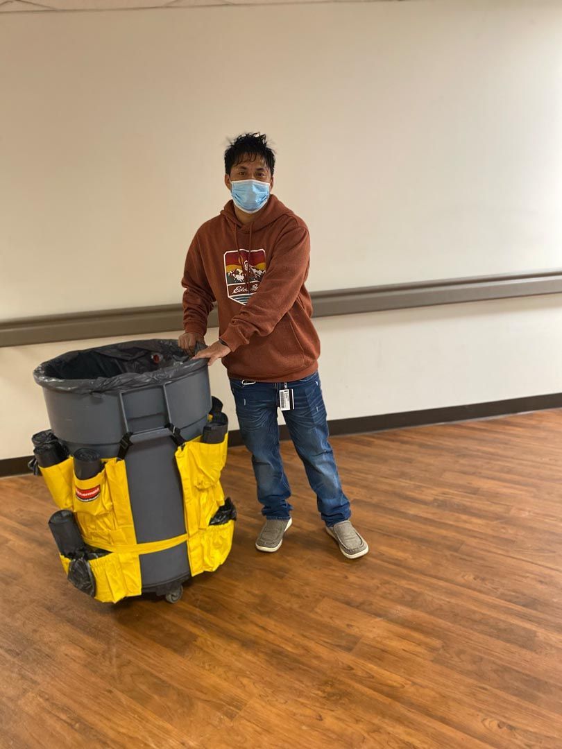 A man wearing a mask is standing next to a large trash can.