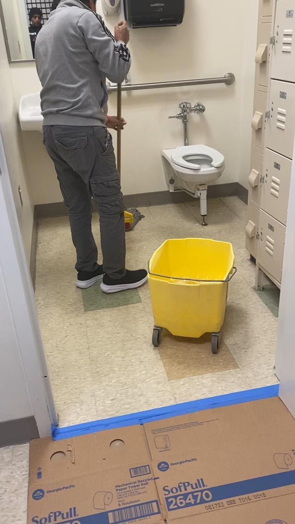 A man is cleaning a bathroom floor with a mop and bucket.