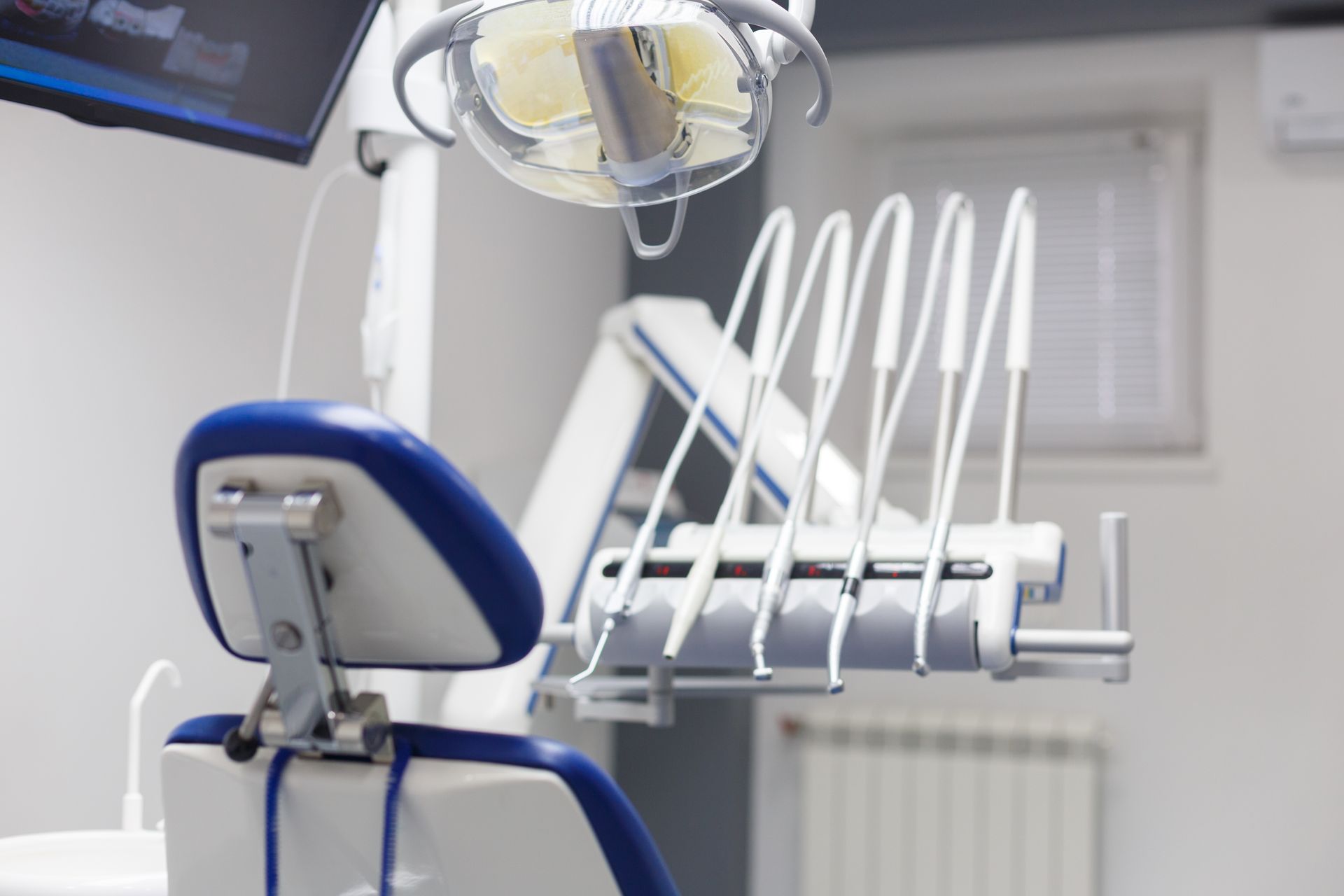 Dental chair with blue and white seat, dental tools, and overhead light in a clinic room.