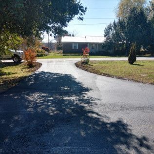Sunny driveway leading to a house, with trees and grass on both sides