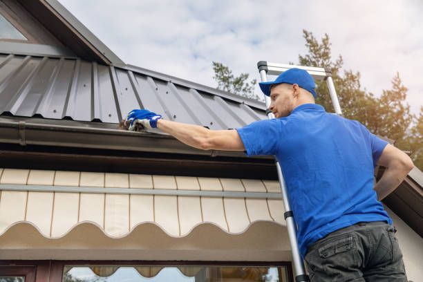 A man is standing on a ladder cleaning moss off the roof of a house.