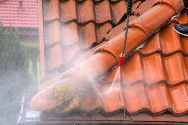 A person is cleaning a tiled roof with a soft pressure washer in Stoke-on-Trent.