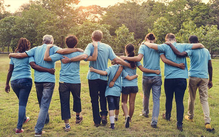 Group of diverse people with arms around each other walking in a park, wearing blue shirts.