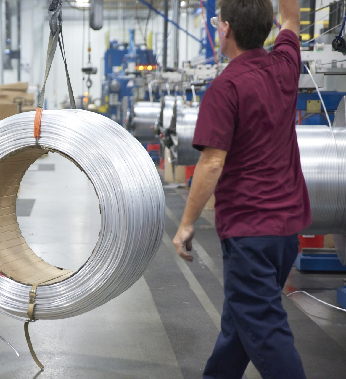 Employee in burgundy shirt at Brazeway, lifting a large spool of aluminum