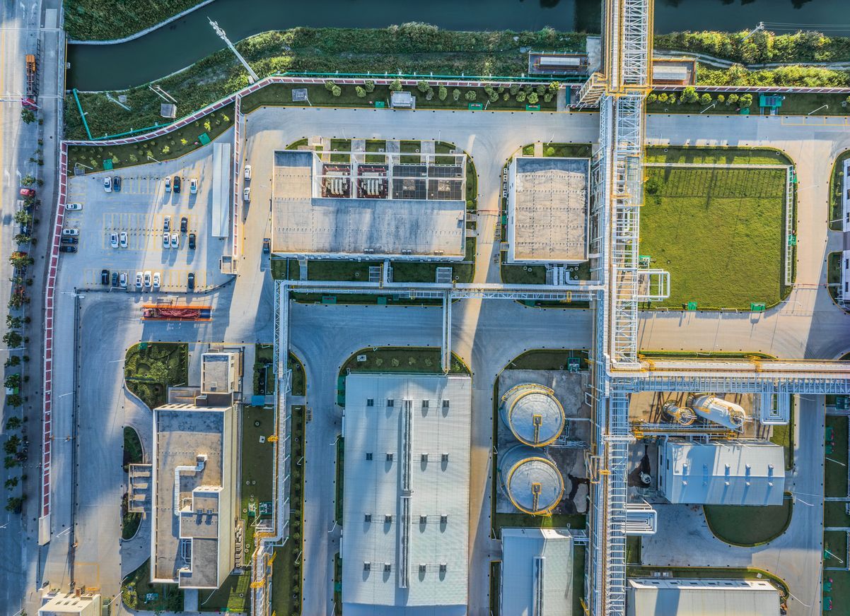 Overhead view of an industrial complex with buildings, tanks, parking, and green areas.