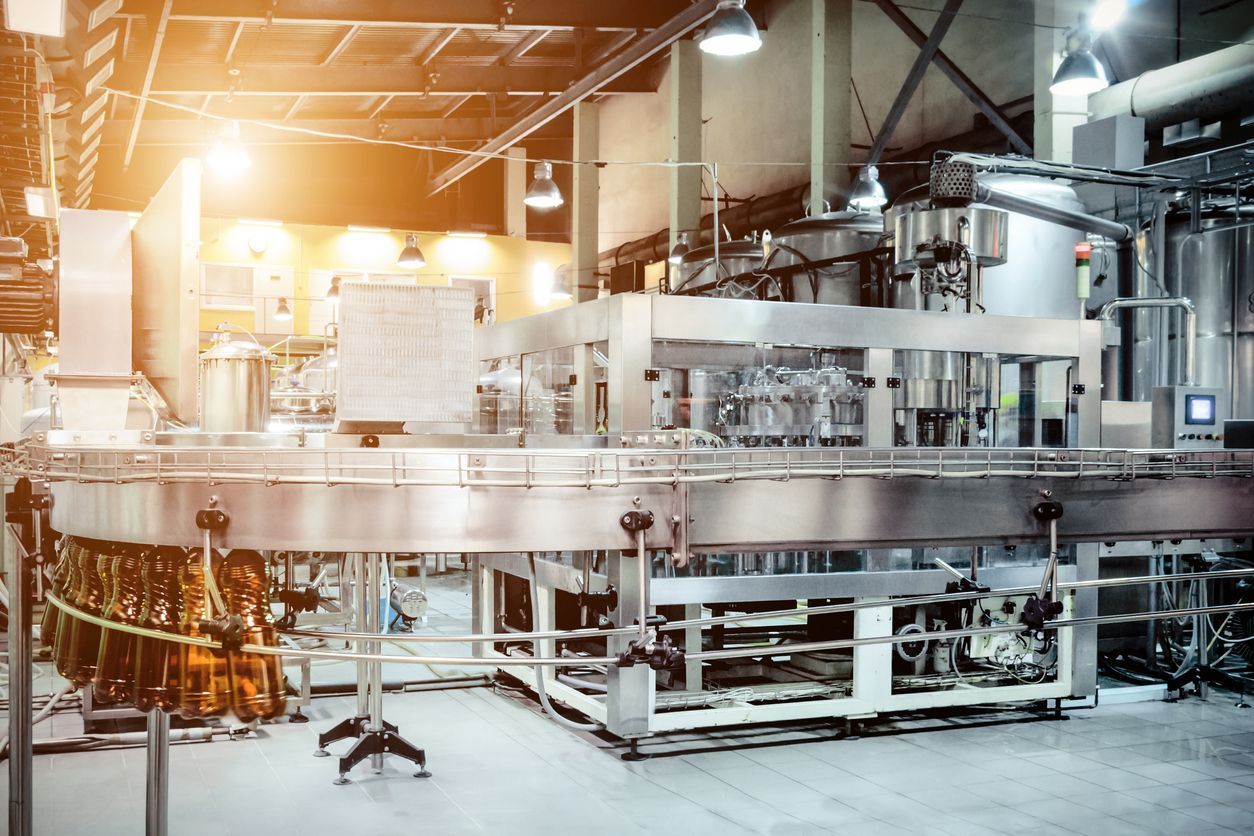 Bottling machine in a factory setting, filling glass bottles with liquid.