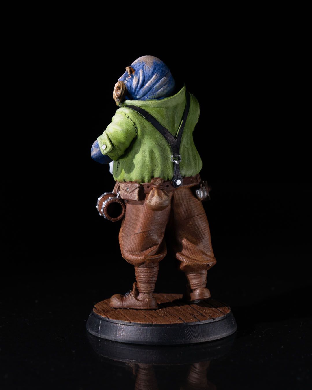 A figurine of a man in a green shirt and brown pants is standing on a wooden base.