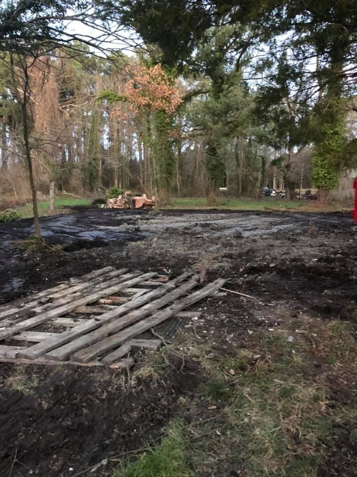 Dark, muddy ground with scattered wooden planks. Trees in background, orange construction vehicle in distance.