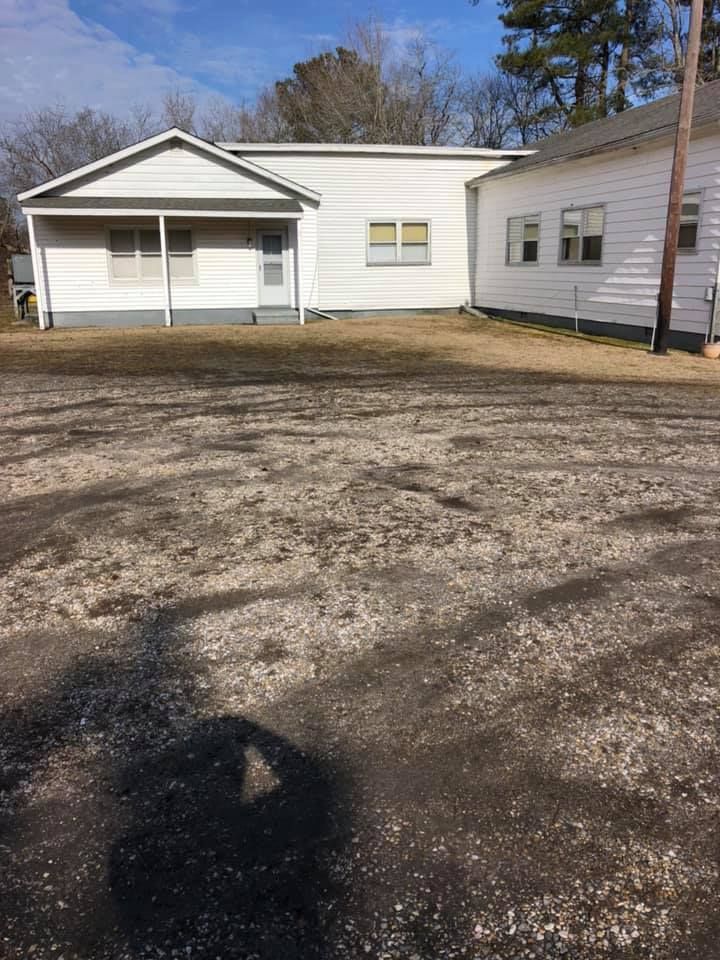 White building with a porch, situated on a gravel lot under a clear sky.