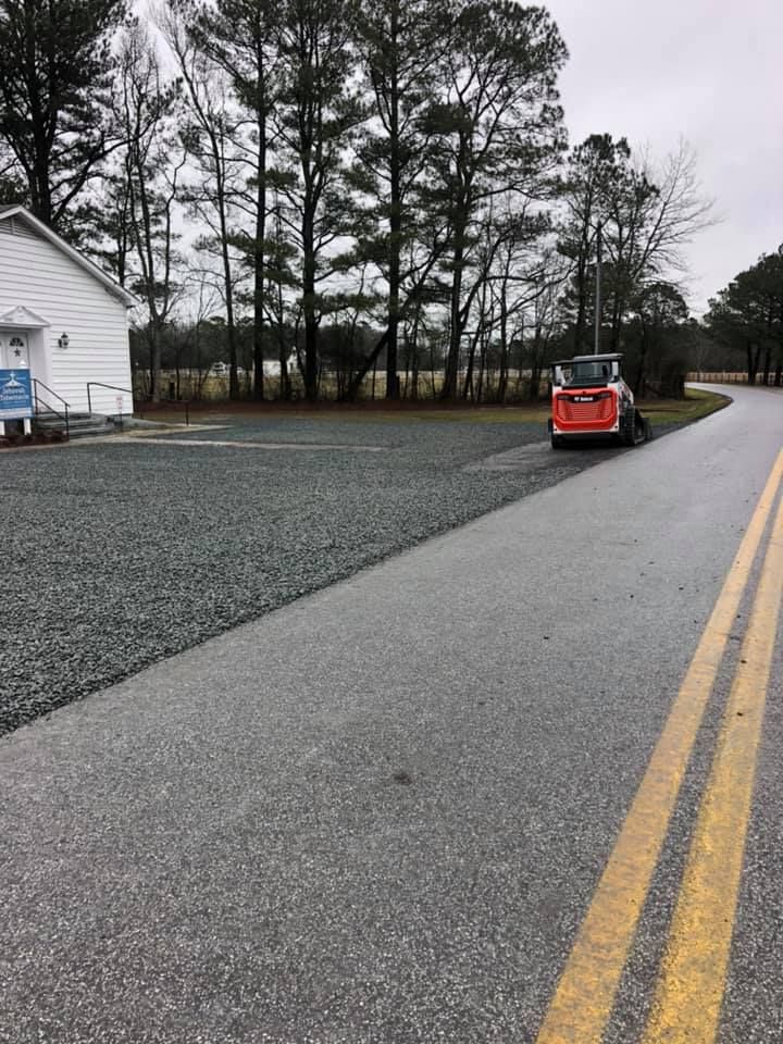 Roadside view: Small building, gravel parking area, and an orange skid steer next to an asphalt road with yellow lines.
