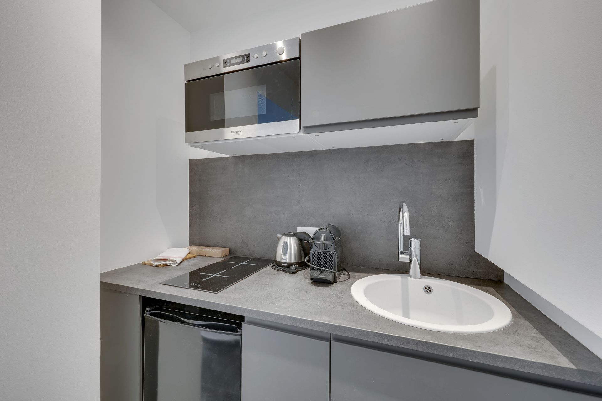 Small kitchenette with gray cabinets, microwave, sink, and mini-fridge.