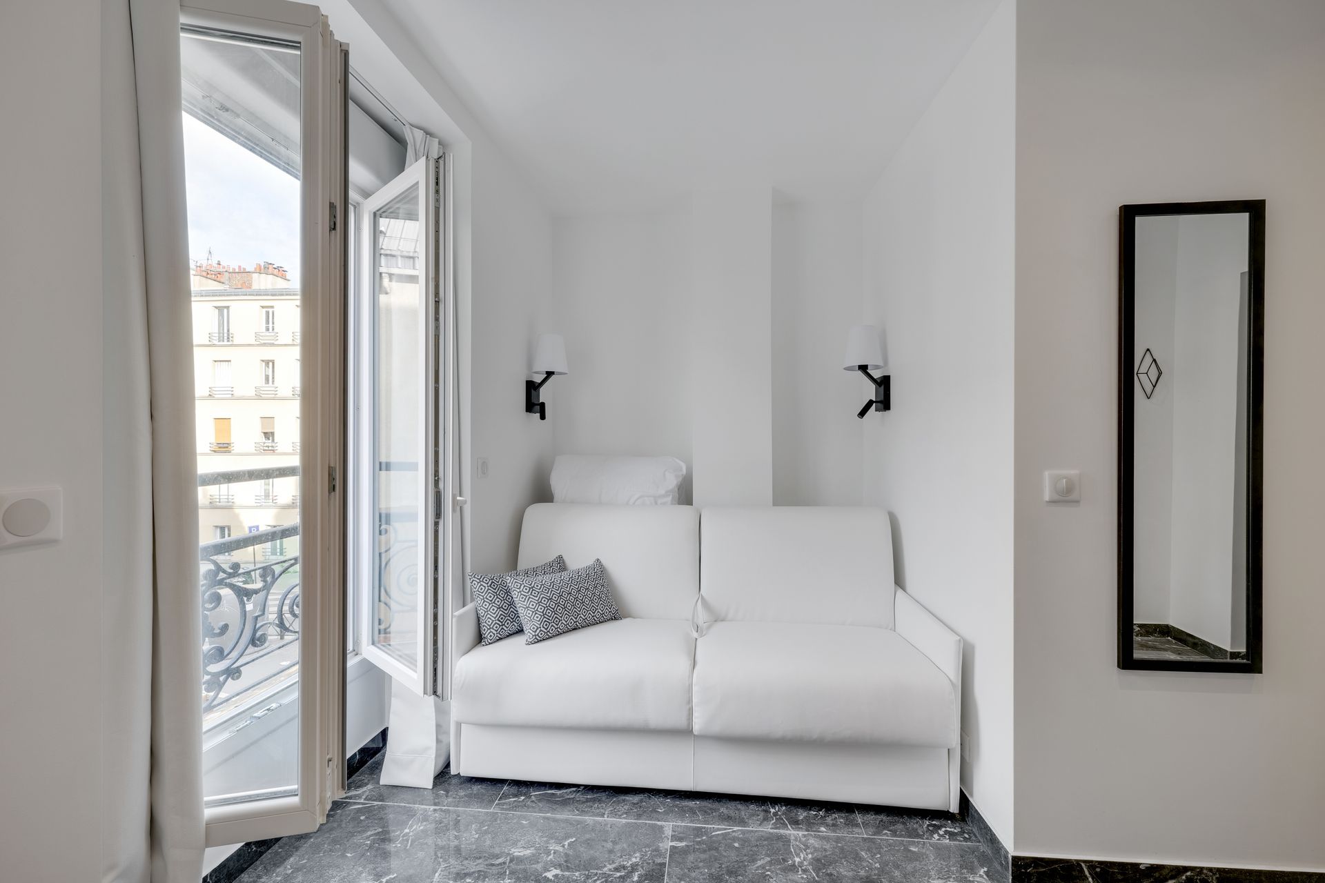 Small, bright white room with a sofa bed, balcony, and mirror.
