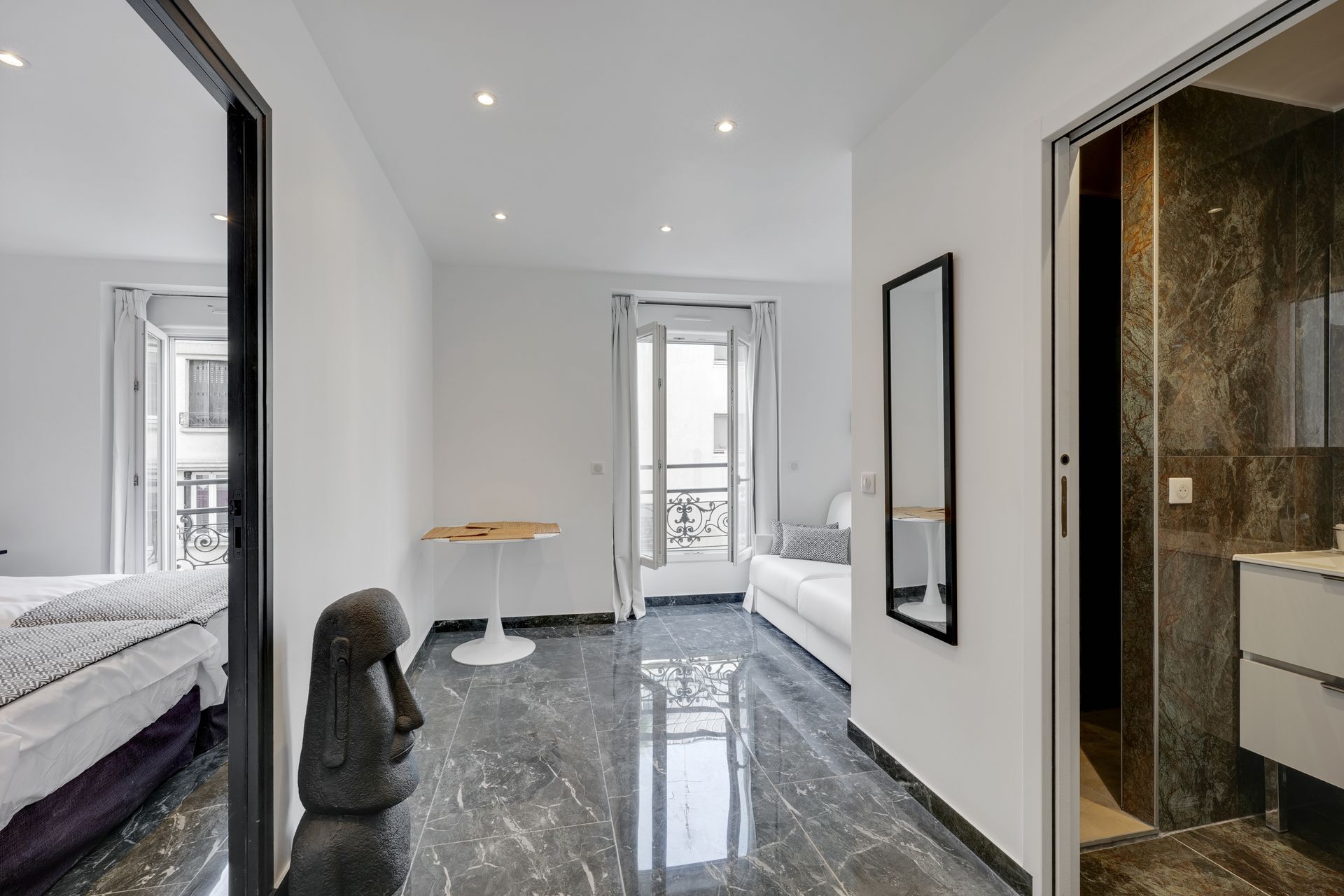 Apartment hallway with marble-like floors, a mirror, a statue, and a view of a balcony.