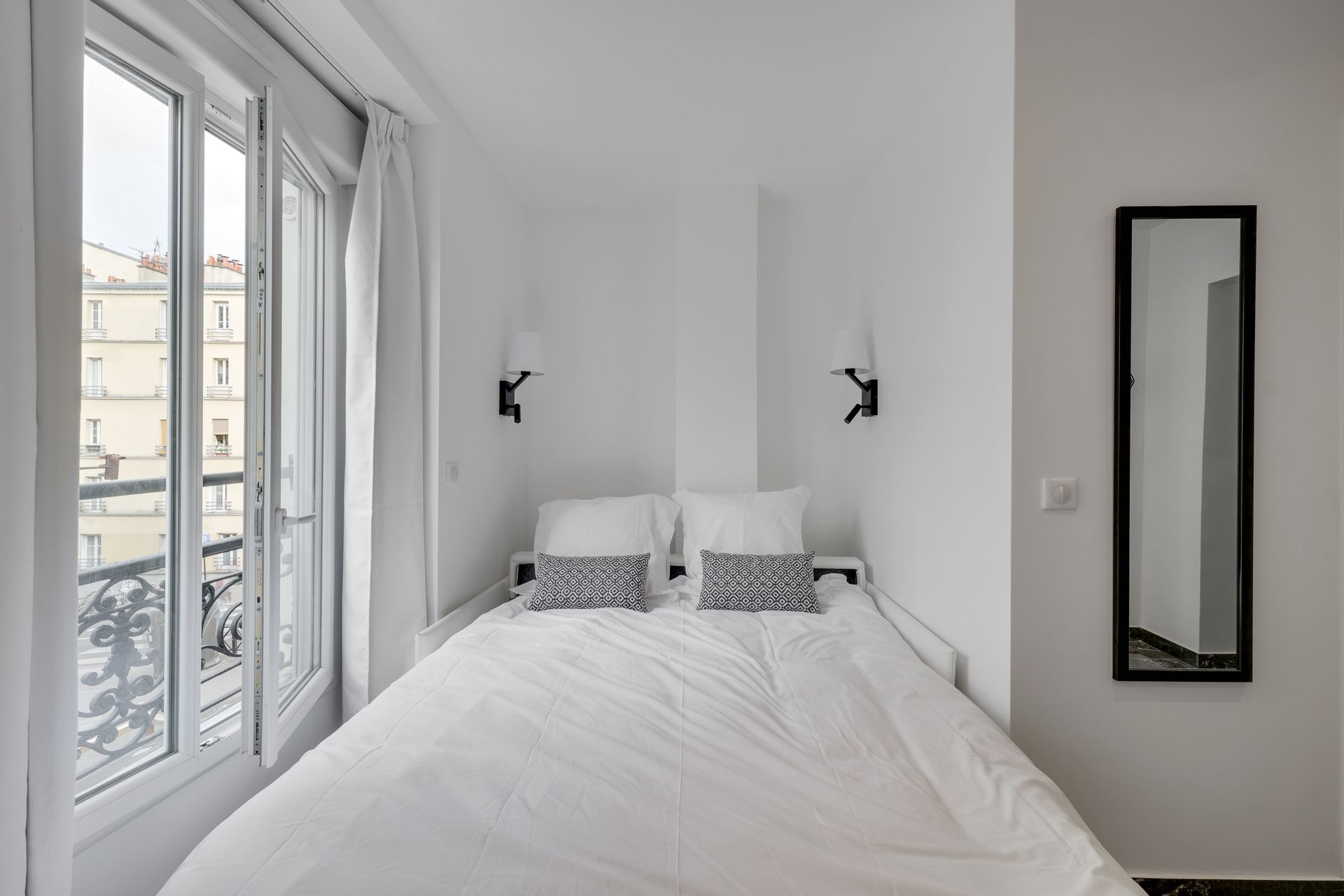 Small, white living room with sofa bed, large window, mirror.