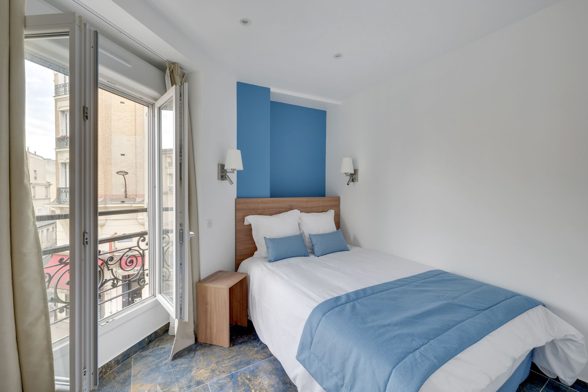 Small bedroom with a double bed, blue and white accents, and a balcony with a city view.