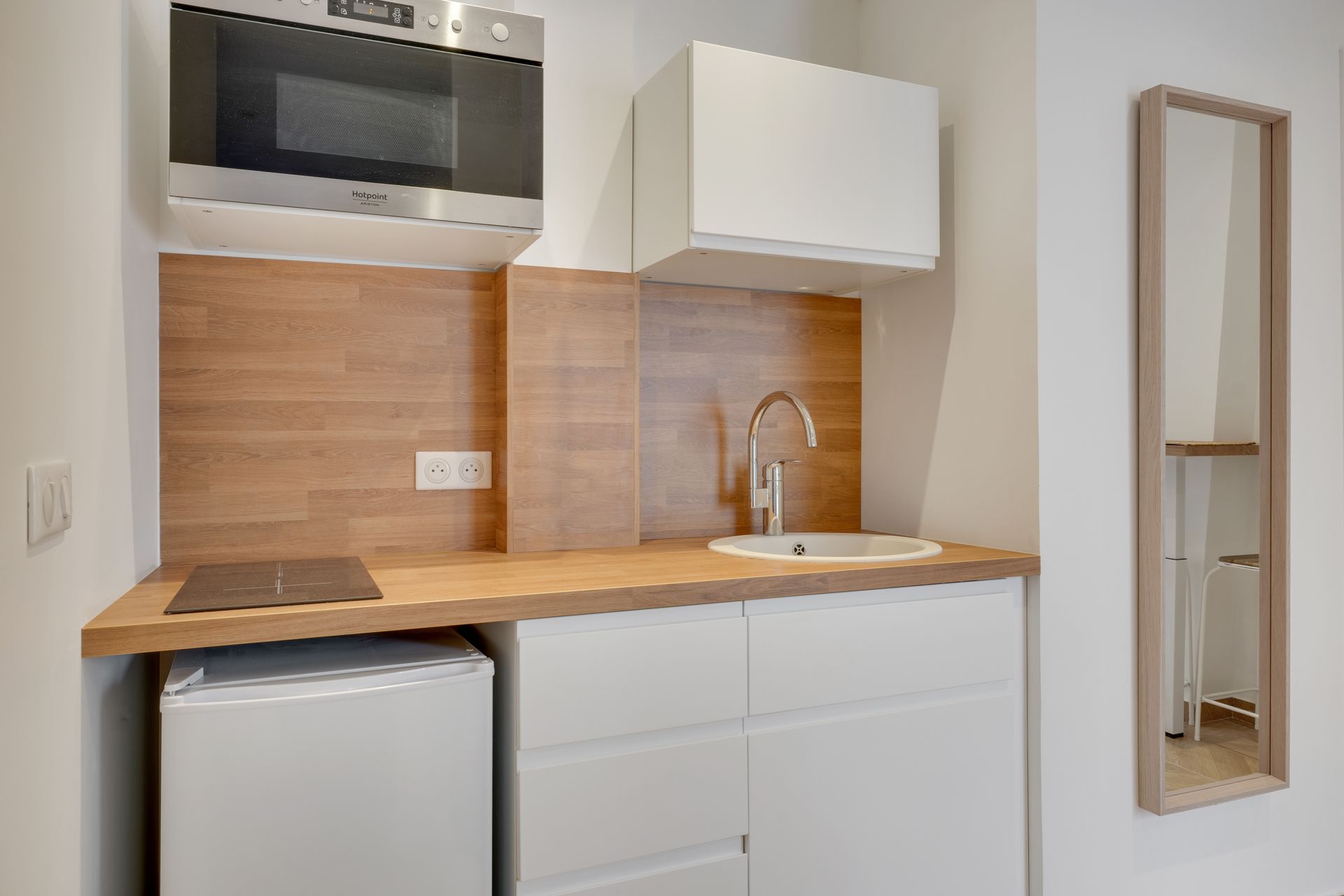 Small white kitchen with a microwave, sink, refrigerator, and a mirror.