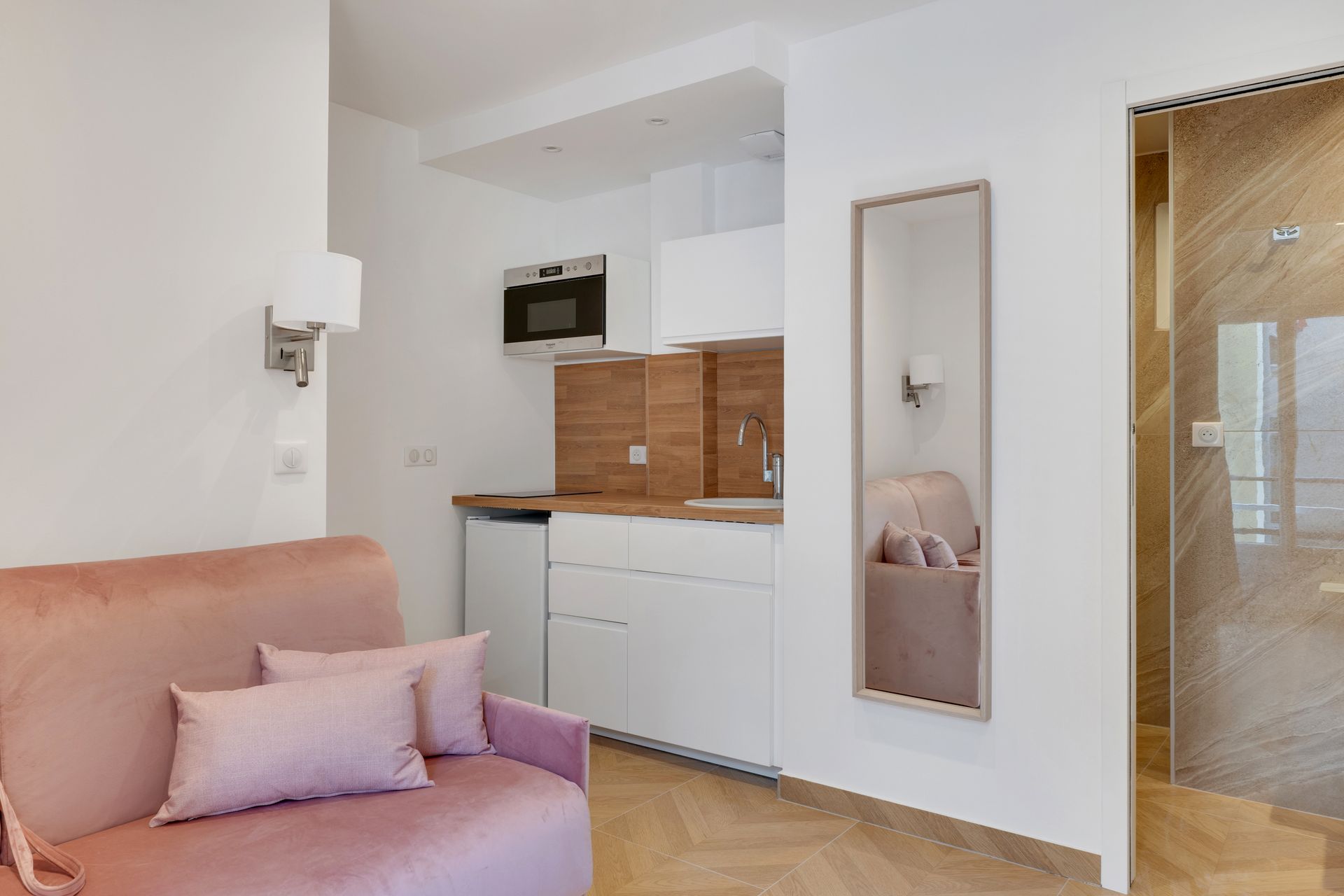 Small, pink sofa bed in a modern apartment with a kitchenette and a full-length mirror.