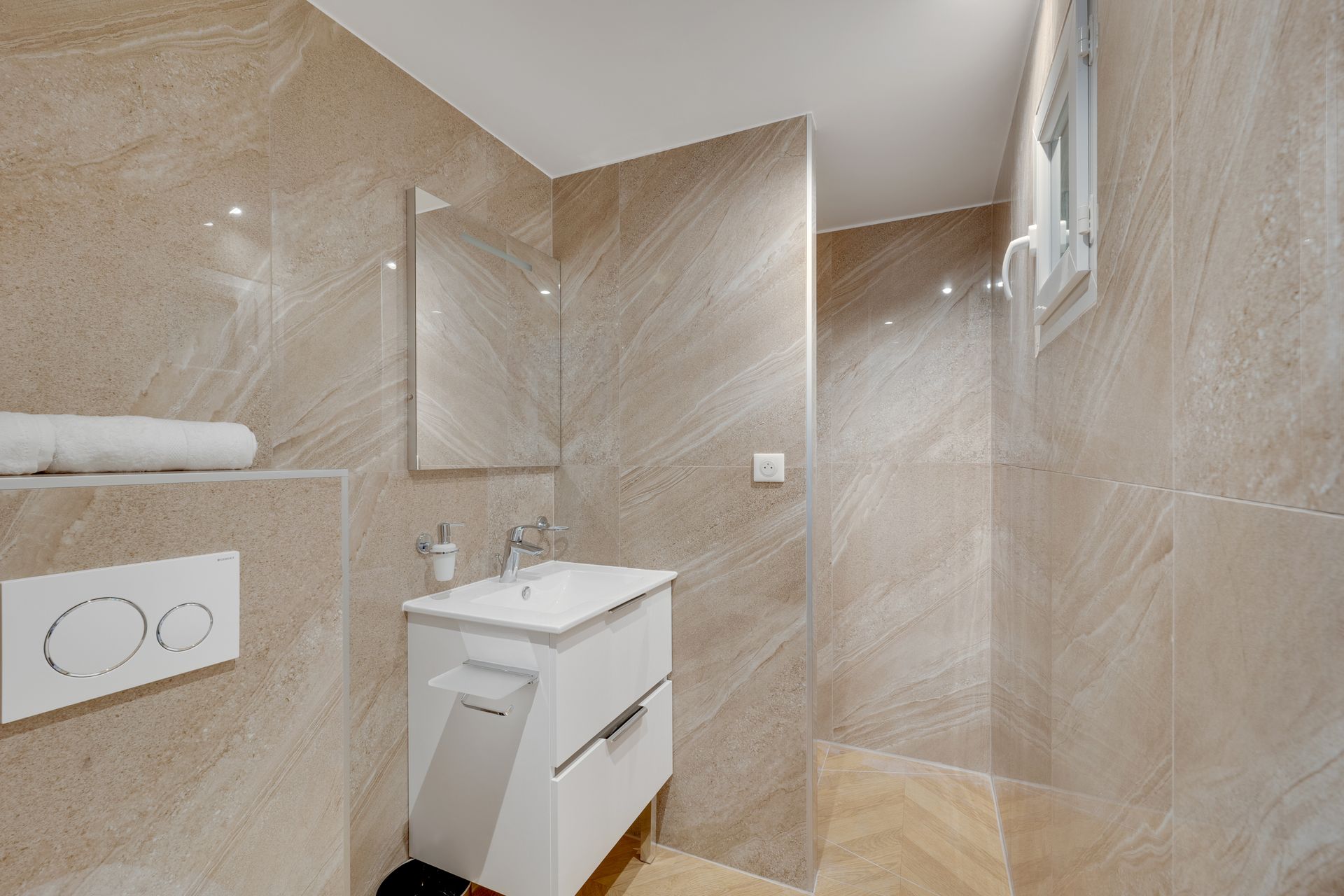 Modern bathroom with beige tiled walls, white sink, and small window.