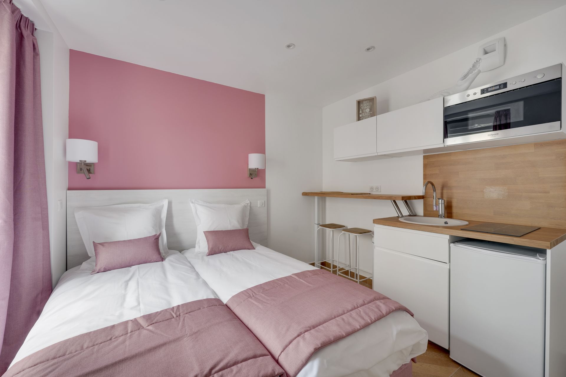 Small pink and white studio with bed and kitchenette.