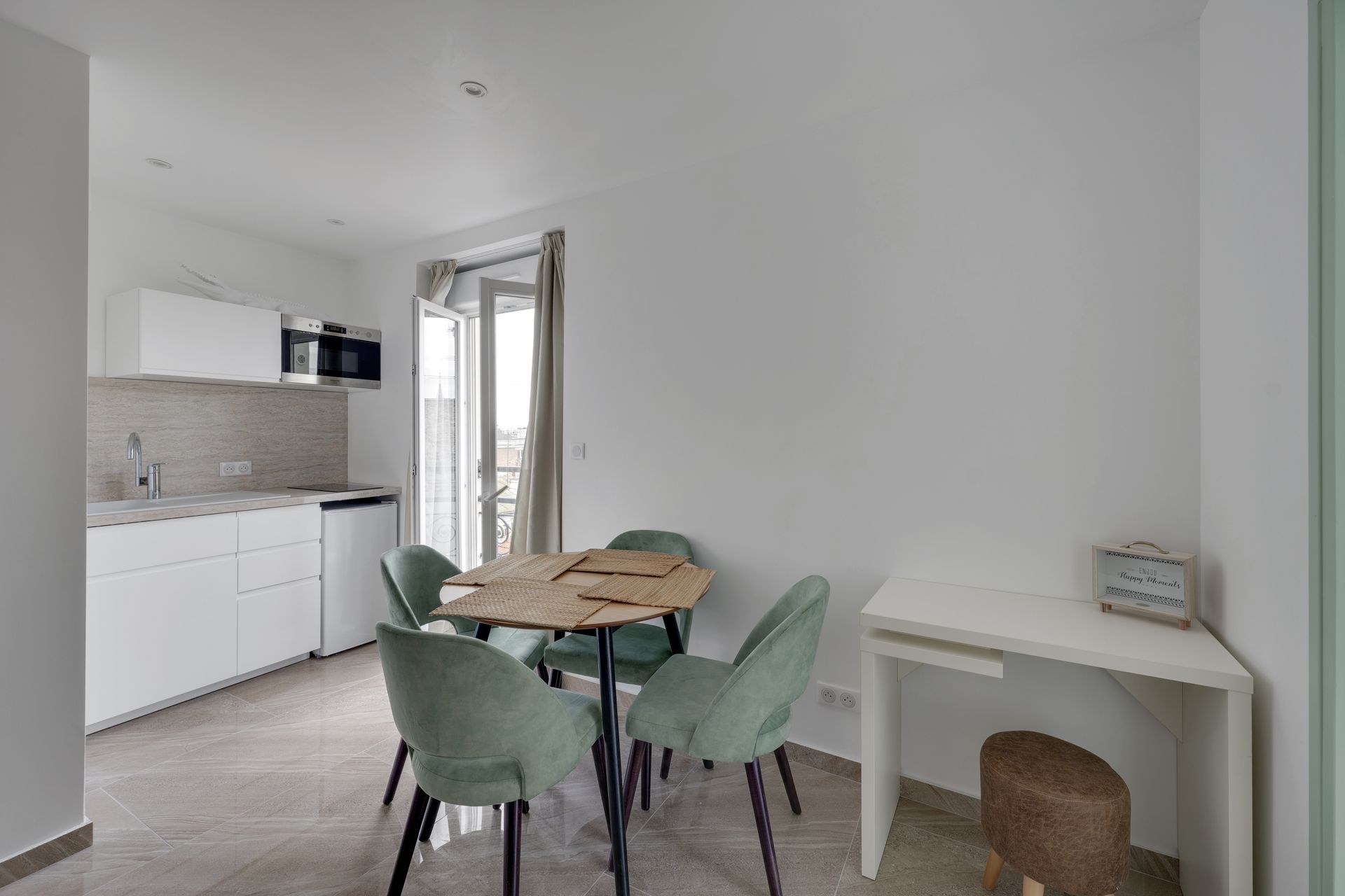 Small, bright dining area with a table, four green chairs, and a small kitchen.