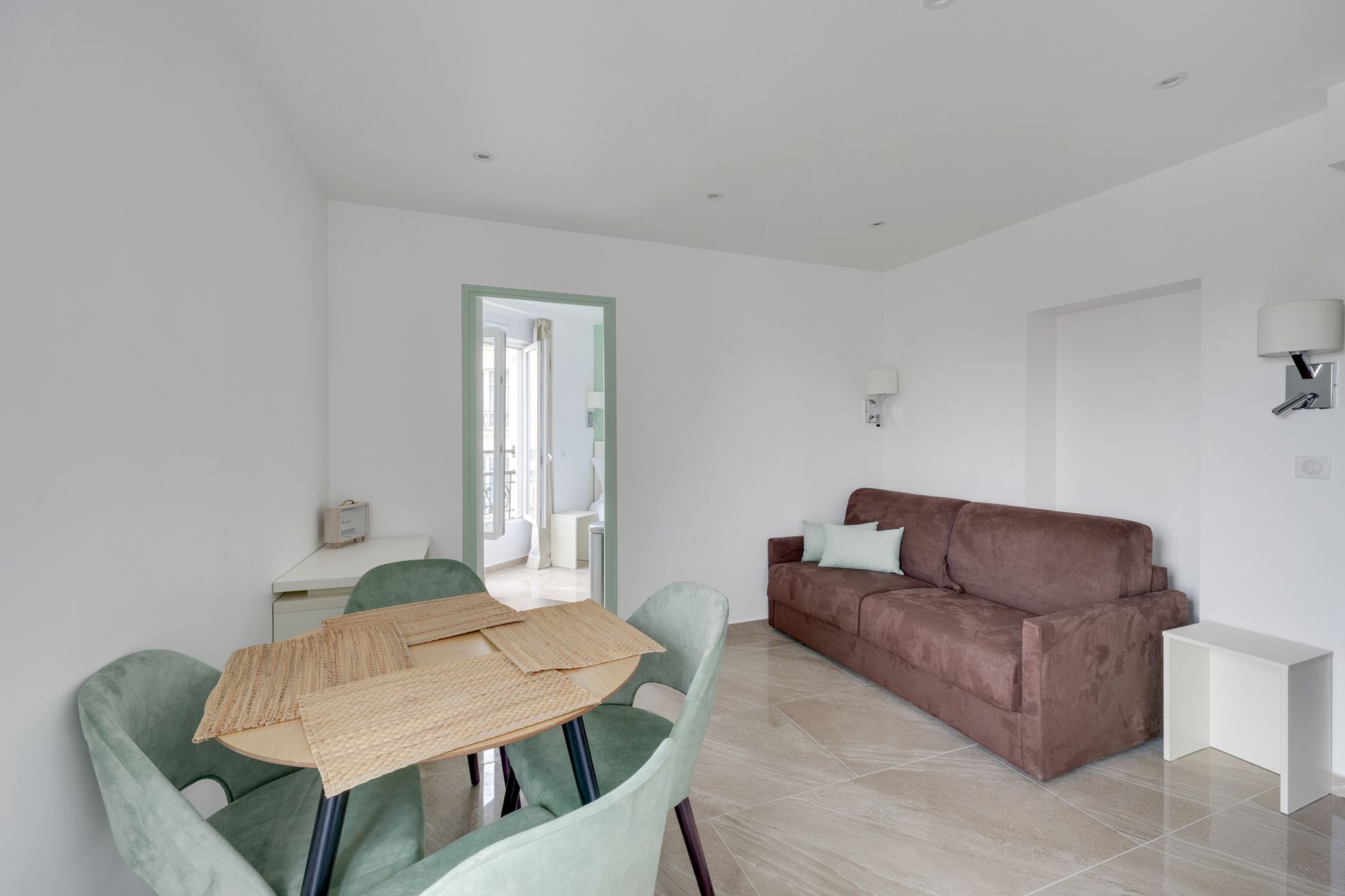 Living room with a brown sofa bed, dining table with chairs, and an open doorway.