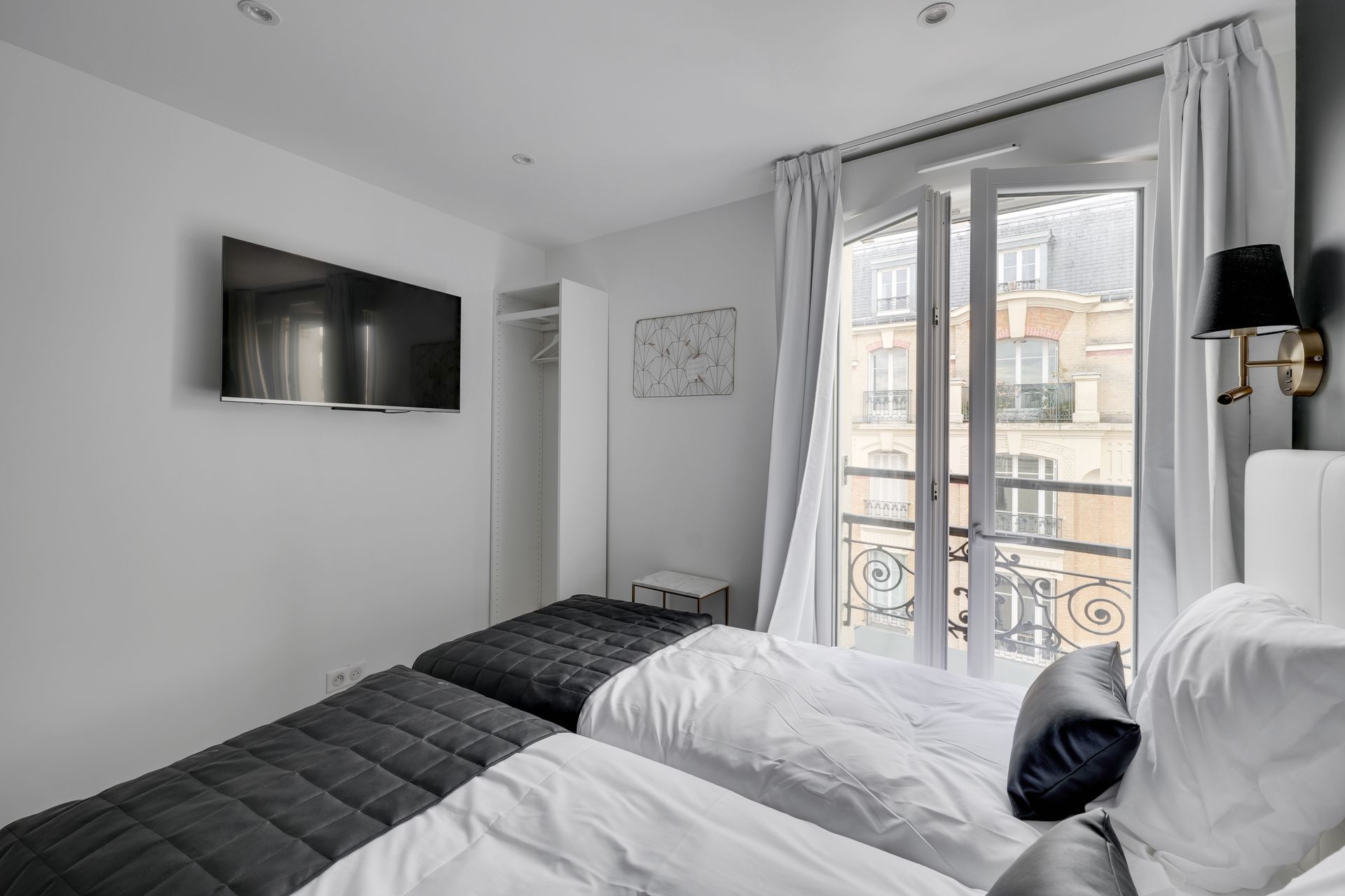 A studio with two twin beds, a TV, and a balcony overlooking a city street.