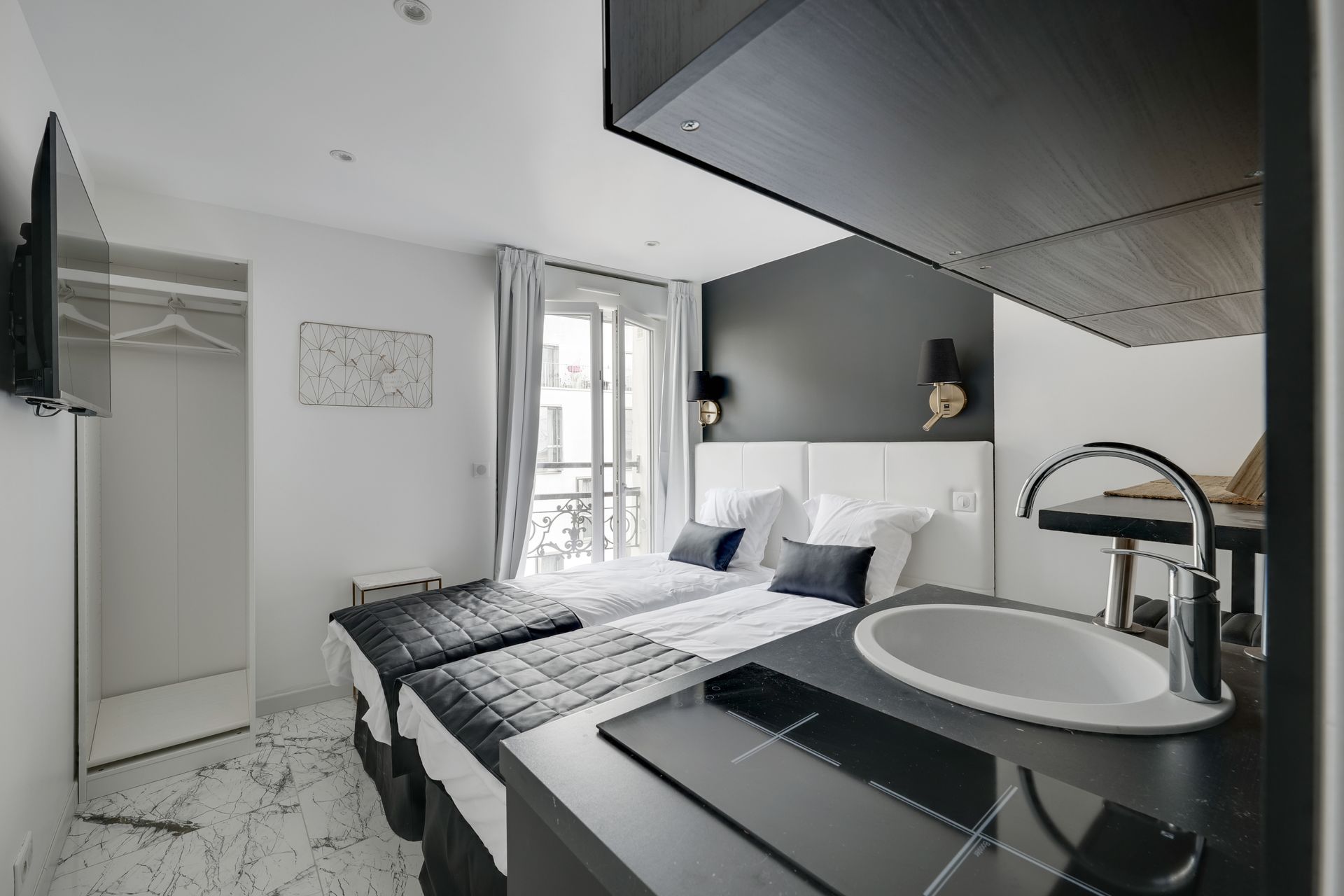 Small studio with two beds, kitchenette, and a window with balcony view.