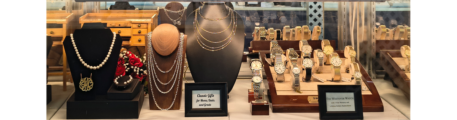 showcase display of pearls, sterling silver & gold chains, and watches labeled Classic Gifts for Moms, Dads, and Grads