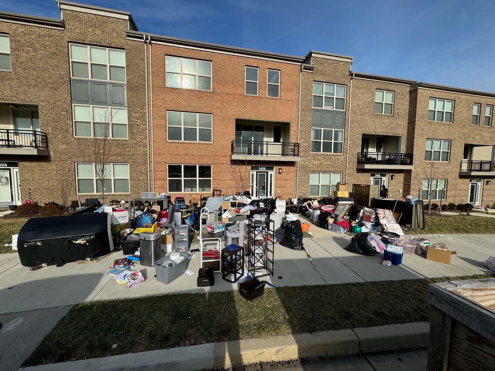 Pile of items on a sidewalk in front of a brick building. Day, clear sky.