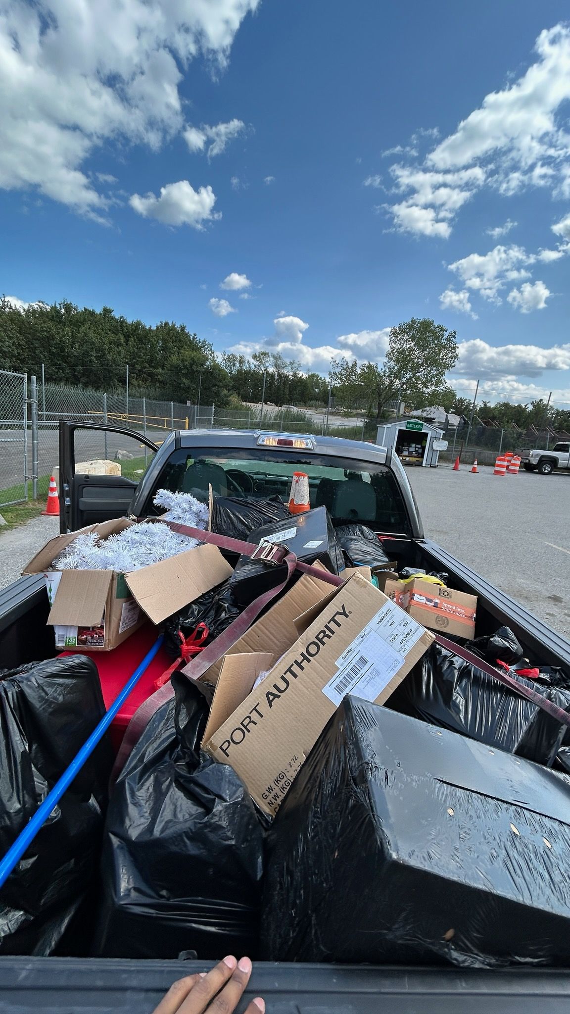 Truck bed filled with trash bags, boxes, and debris, under a sunny blue sky.