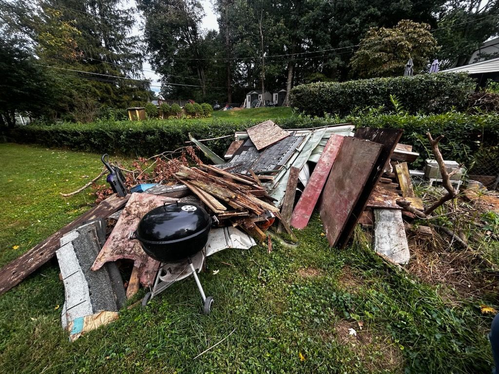 A pile of construction debris with a black grill on a lawn; trees and bushes in the background.
