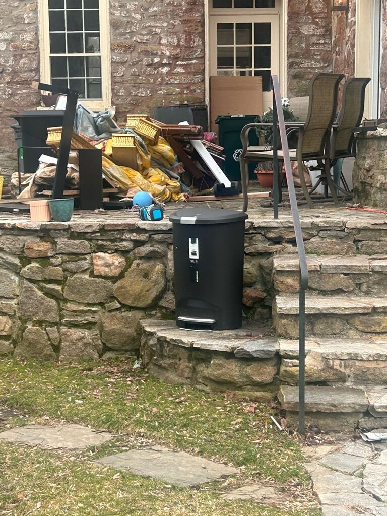 Black trash can on stone steps, debris on patio behind it.