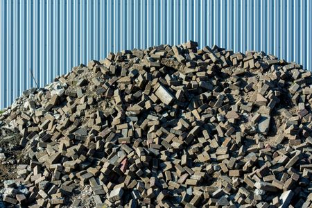 Pile of broken bricks in front of a corrugated metal wall.