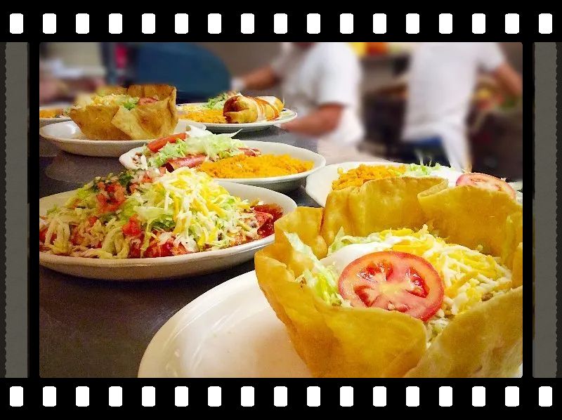 Tacos and other Mexican food on plates, featuring a taco salad with a tomato slice.