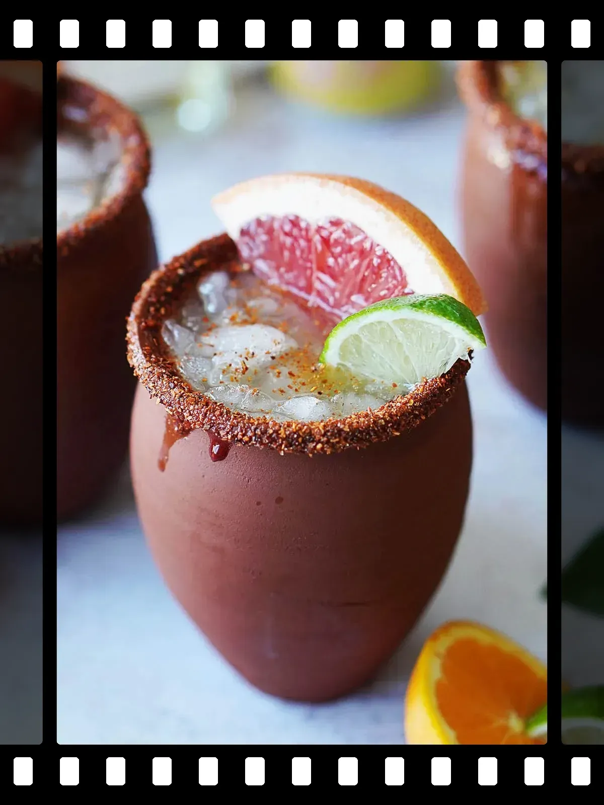 Cocktail in clay cup with citrus garnish and spiced rim.