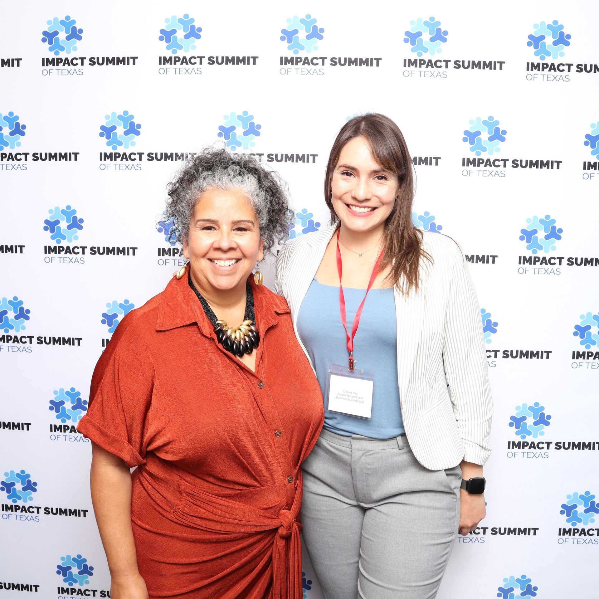 Two women are posing for a picture in front of a wall that says impact summit.