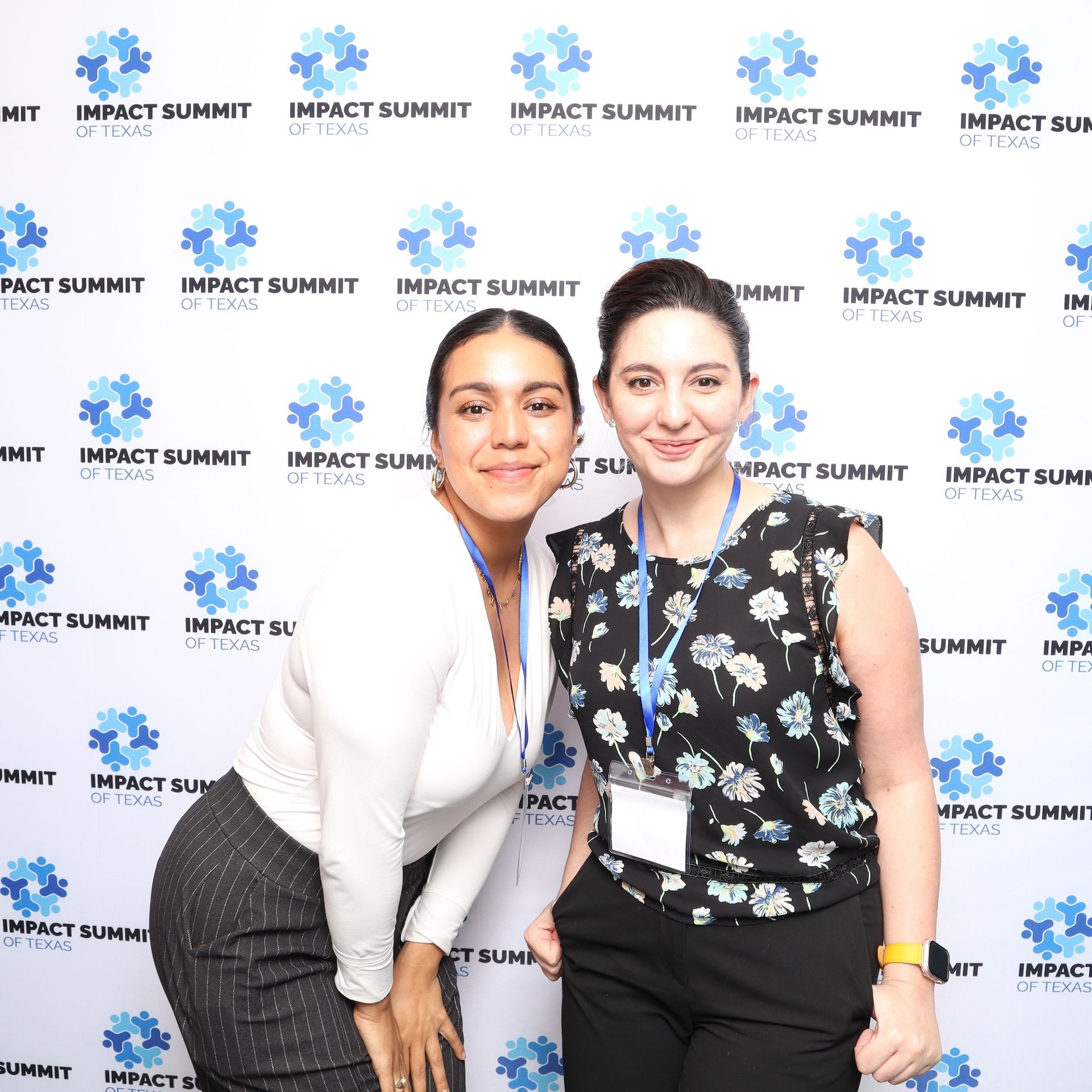 Two women are posing for a picture in front of a wall that says impact summit.