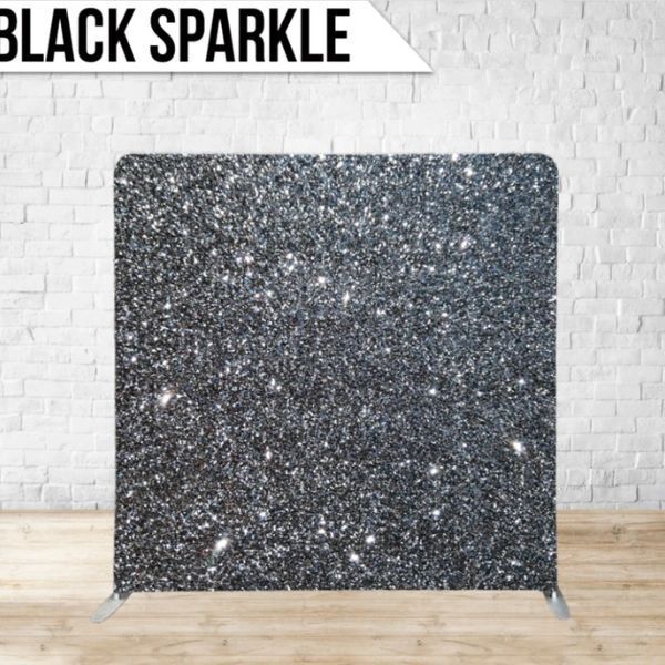 A black sparkle backdrop is sitting on a wooden floor in front of a white brick wall.